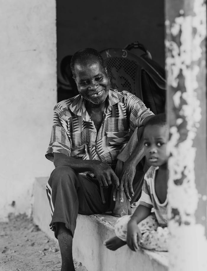 Black and white image of an elderly man with a young child sitting on a porch, conveying warmth.