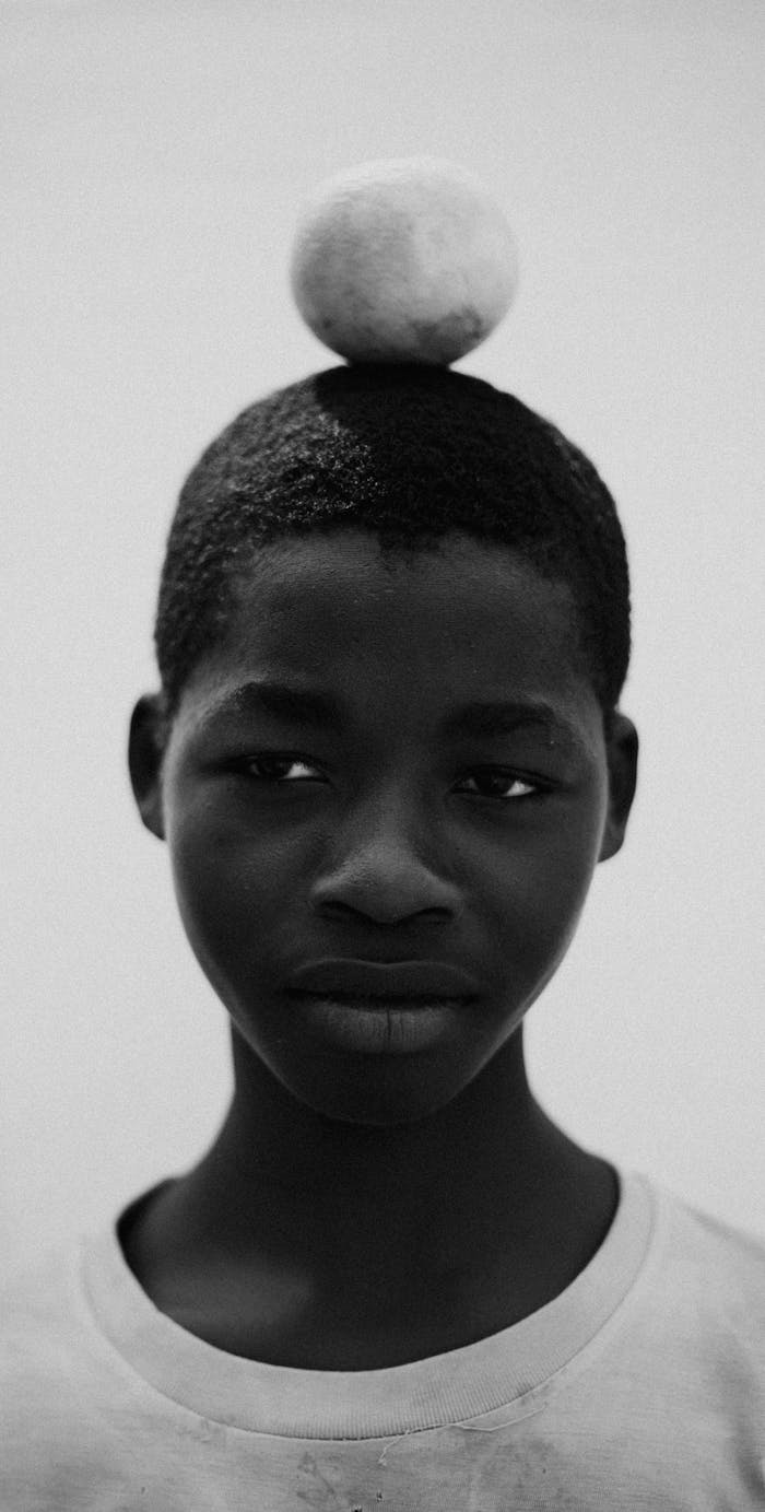 Artistic portrait of a teenager balancing a fruit on head in black and white.