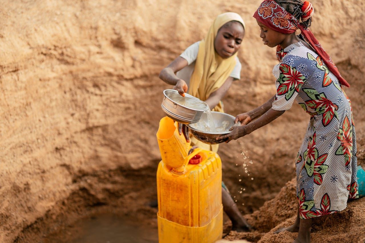 Two children collecting water in a rural area using jerry cans.