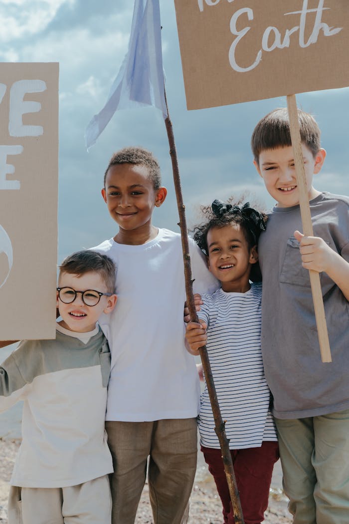 Group of diverse children smiling and holding environmental signs outdoors under a clear sky.